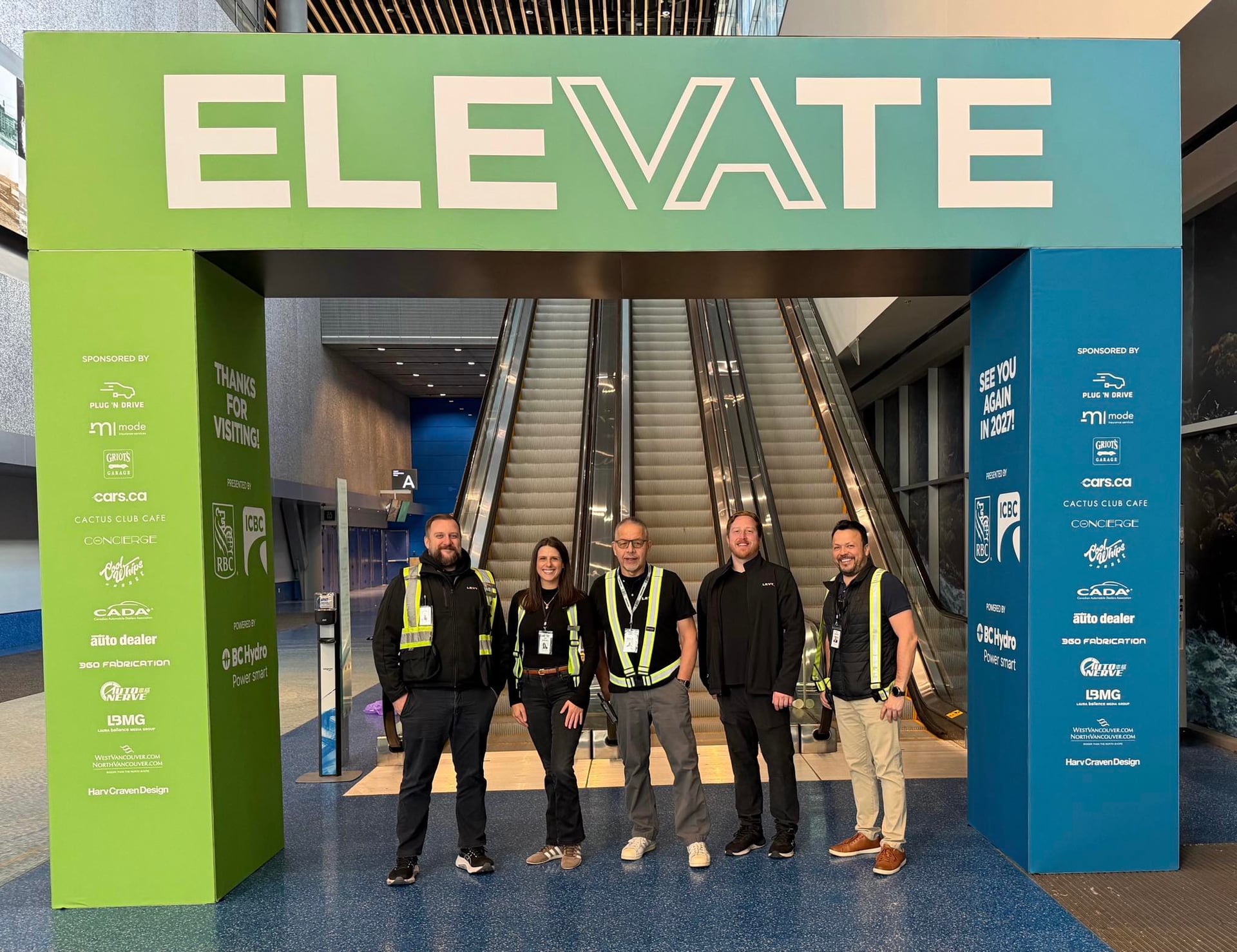 Five members of the LEVY crew standing under the green ELEVATE entrance archway they built at the Vancouver Convention Centre.